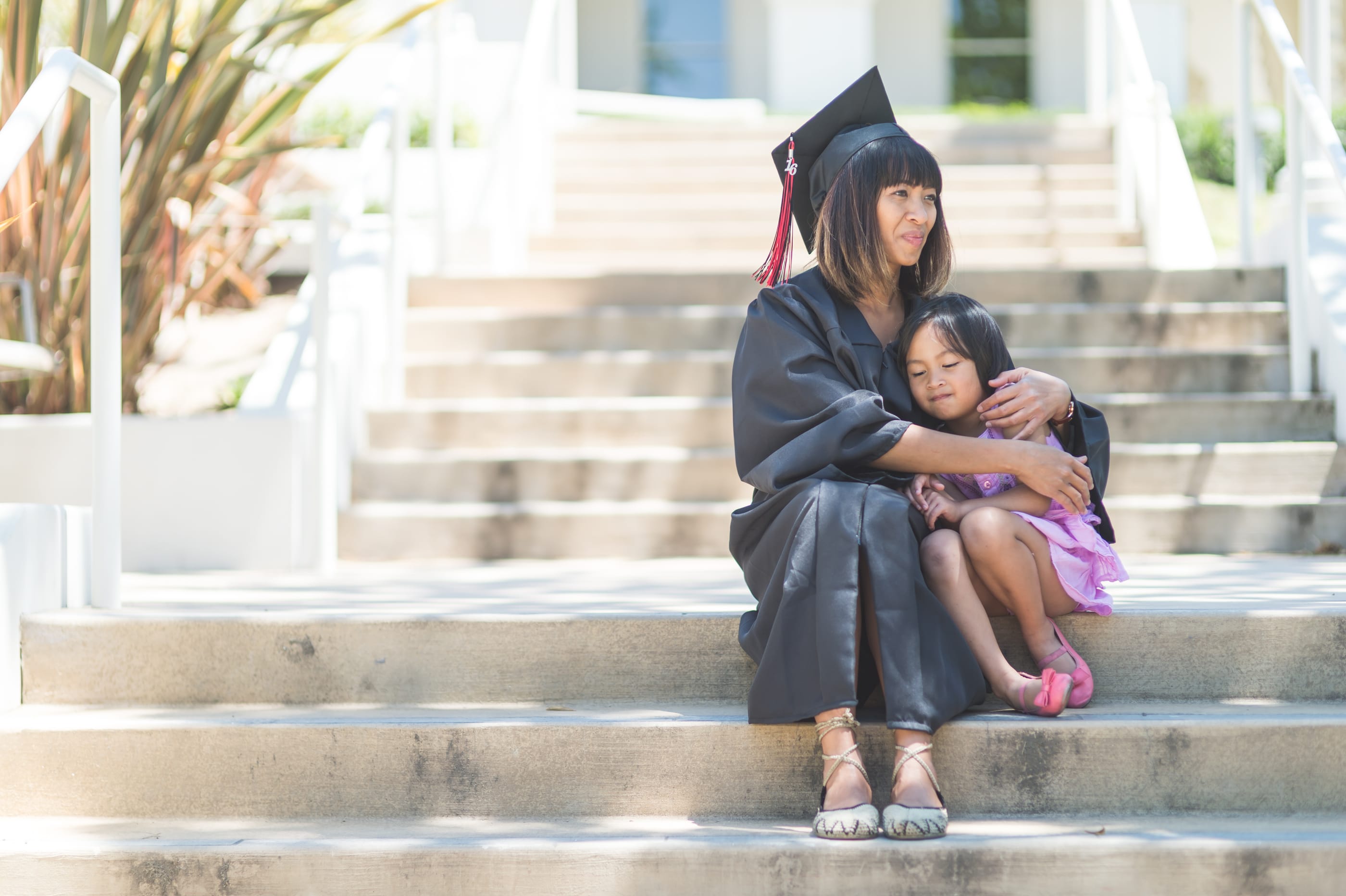 Woman wearing a graduation cap and robe hugging her daughter