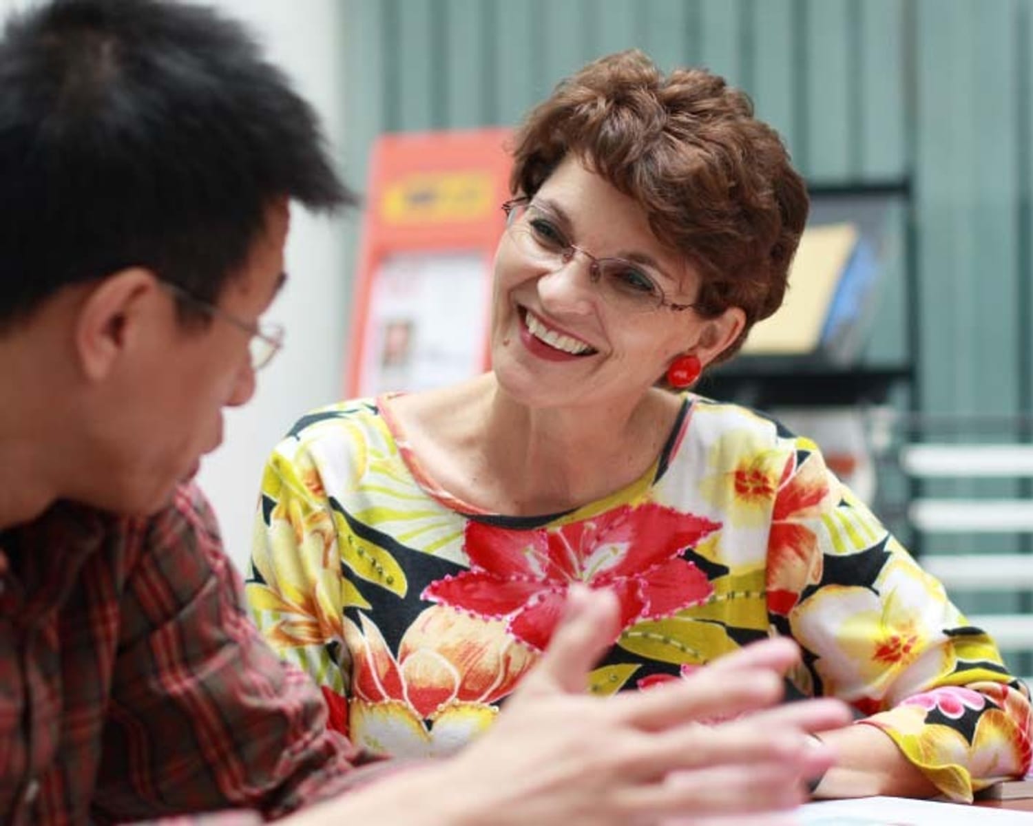 Woman smiling as she looks towards student who is gesturing as he talks with his hands