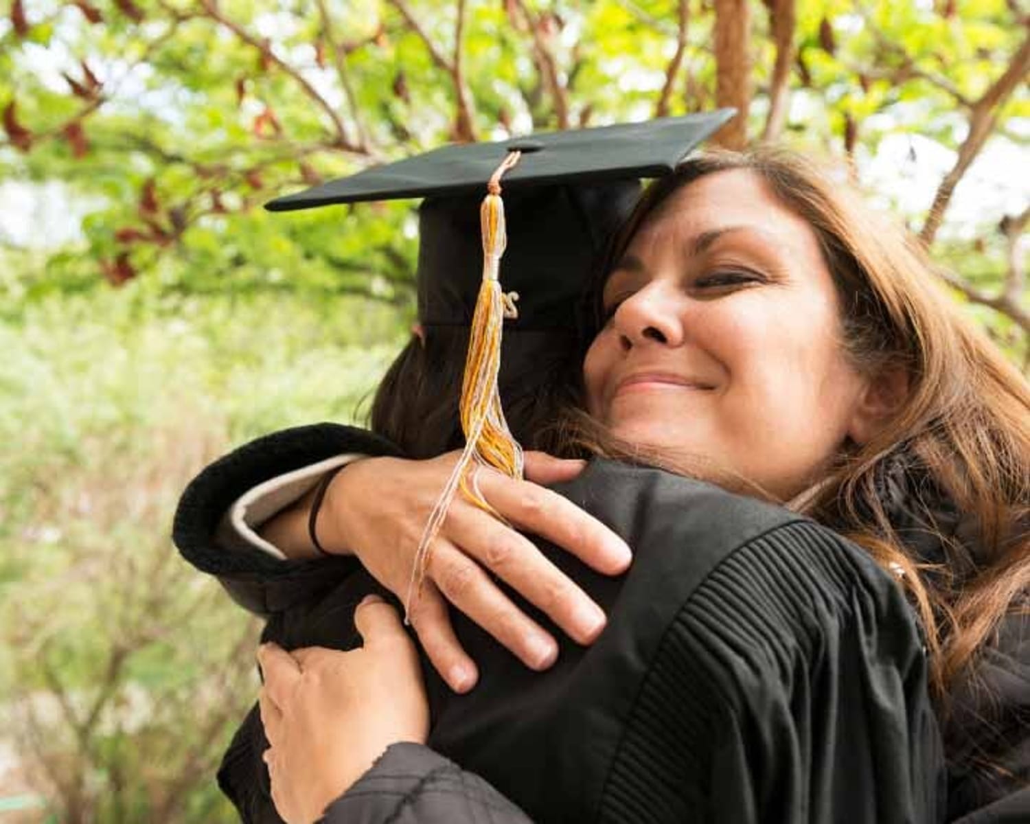 Una figura materna mirando a la cámara mientras abraza a su hija con un birrete y un vestido de graduación